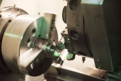 Obróbka precyzyjna na tokarce CNC. Narzędzie tnie metalowy element, tworząc skomplikowany kształt. Proces ten jest kluczowy dla produkcji części maszyn, np. w branży lotniczej, gdzie liczy się każdy detal, jak w przypadku modelu dn80.