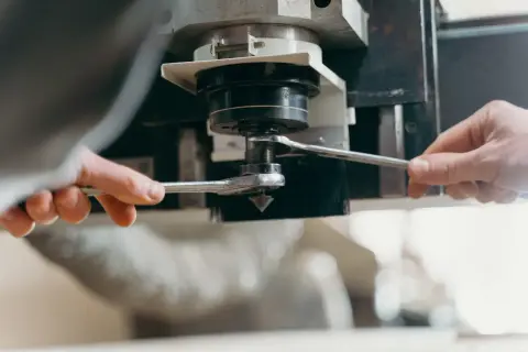 Dwie ręce dokręcają kluczem element maszyny CNC, przygotowując ją do pracy z optymalną prędkością skrawania.