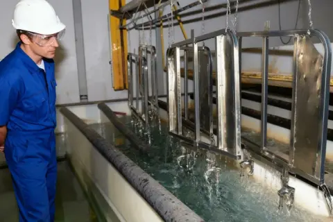 Pracownik w galwanizerni nadzoruje proces zanurzania metalowych elementów w kąpieli. To właśnie galwanizernia, gdzie metale zyskują ochronną powłokę.