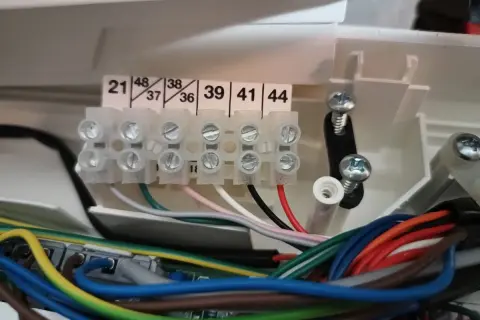 Zaciski elektryczne z numerowanymi wejściami i wiązką kolorowych przewodów.