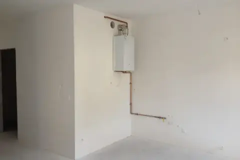 Widok na pomieszczenie, gdzie widać jak zabudować piec gazowy. Biały piec wiszący na ścianie, połączony miedzianymi rurkami z instalacją.