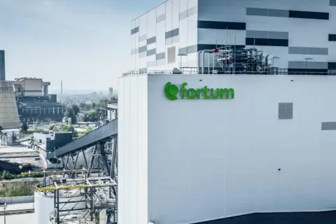 Nowoczesna elektrociepłownia Fortum z zielonym logo, w tle kominy i chłodnia kominowa.