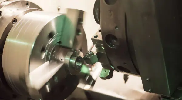 Obróbka precyzyjna na tokarce CNC. Narzędzie tnie metalowy element, tworząc skomplikowany kształt. Proces ten jest kluczowy dla produkcji części maszyn, np. w branży lotniczej, gdzie liczy się każdy detal, jak w przypadku modelu dn80.