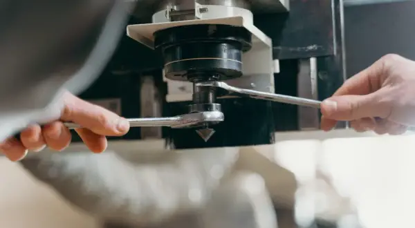 Dwie ręce dokręcają kluczem element maszyny CNC, przygotowując ją do pracy z optymalną prędkością skrawania.