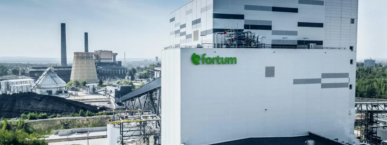 Nowoczesna elektrociepłownia Fortum z zielonym logo, w tle kominy i chłodnia kominowa.