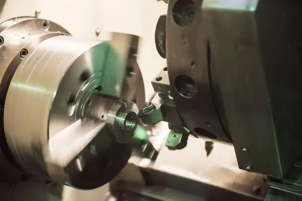 Obróbka precyzyjna na tokarce CNC. Narzędzie tnie metalowy element, tworząc skomplikowany kształt. Proces ten jest kluczowy dla produkcji części maszyn, np. w branży lotniczej, gdzie liczy się każdy detal, jak w przypadku modelu dn80.